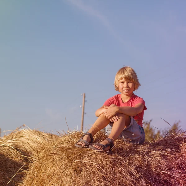 Jongen zittend op een hooiberg — Stockfoto