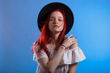 Mavi arka planda siyah şapkalı, kızıl saçlı güzel bir kadının portresi..