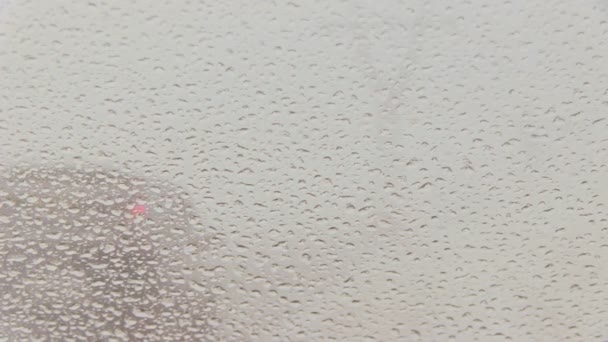 Traffic viewed through a car windscreen covered in rain, focus on raindrops — Stock Video