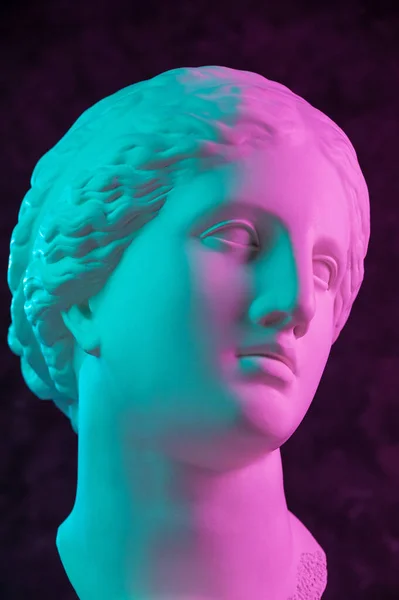 Colorful gypsum copy of ancient statue of Venus de Milo head for artists on dark textured background. Plaster sculpture woman face. Art poster in violet and green bright colors. Love, beauty, feminism Royalty Free Stock Images