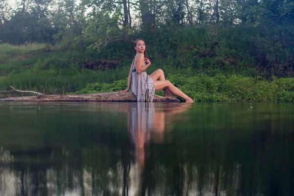 Menina bonita em vestido de algodão está sentado no log — Fotografia de Stock