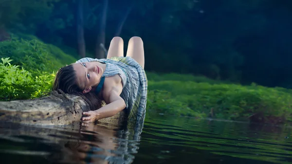 Bella ragazza in abito di cotone è sdraiato sul tronco — Foto Stock