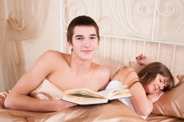 Hombre leyendo un libro y mujer durmiendo a su lado . — Foto de Stock