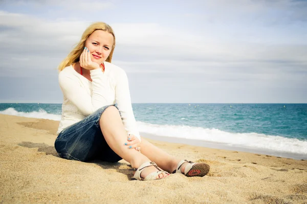 Mulher sentar-se na praia junto ao mar vestindo jeans — Fotografia de Stock