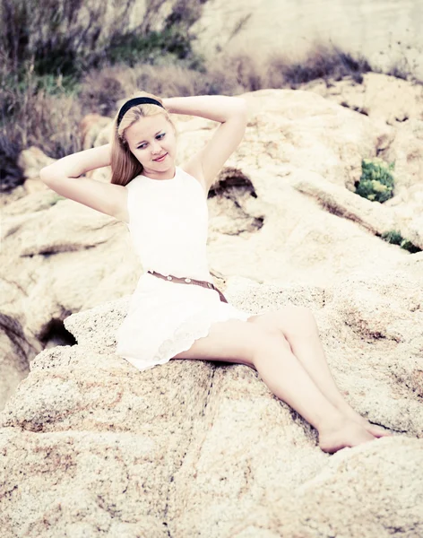 Beautiful young woman sitting on the stone on the seashore — Stock Photo, Image