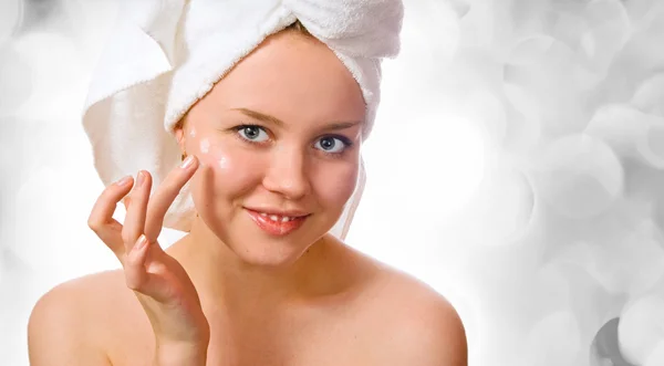 Beautiful woman in towel applying cream after bath with lights in the background — Stock Photo, Image