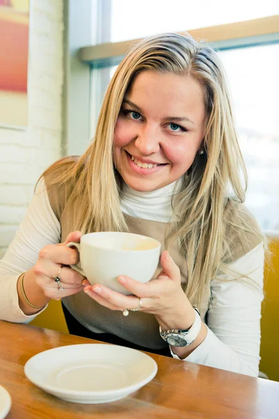 Jonge vrouw drinken koffie uit een witte kop glimlachend — Stockfoto