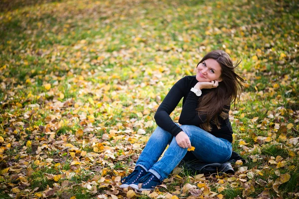 秋の公園で葉の上に座っている若い女性 — ストック写真