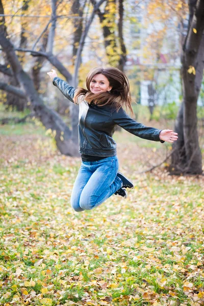 Девушка в черной куртке прыгает в парке осенью — стоковое фото