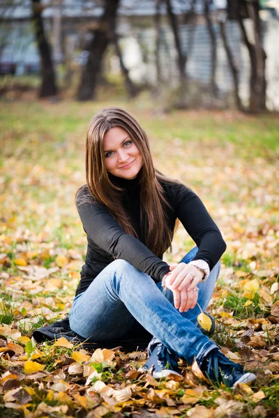 Mujer joven se sienta en hojas en el parque de otoño —  Fotos de Stock