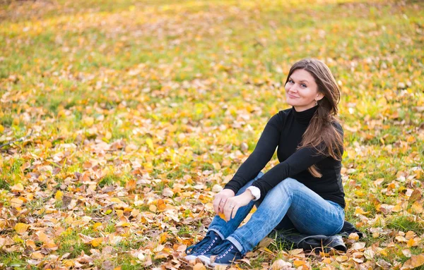 Ung kvinna sitter på bladen i höst park — Stockfoto