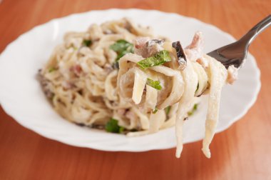 spagetti. Fettuccine carbonara beyaz bir kase, sosis, mantar ve maydanoz ile süslenmiş.
