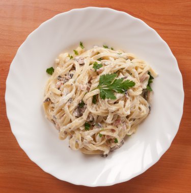 spagetti. Fettuccine carbonara beyaz bir kase, sosis, mantar ve maydanoz ile süslenmiş.