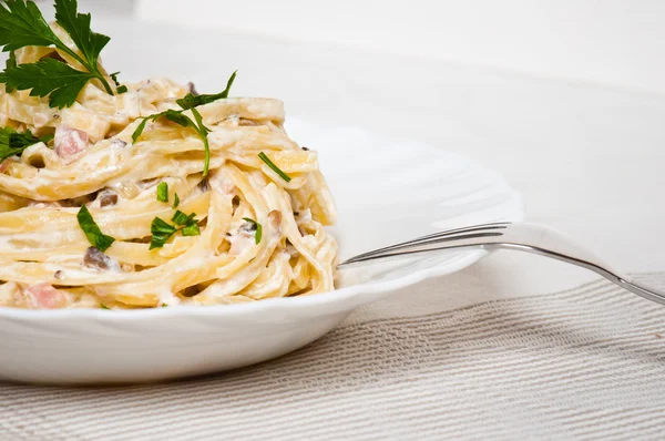 Espaguete. Fettuccine carbonara em uma tigela branca, decorada com bacon, cogumelos e salsa — Fotografia de Stock