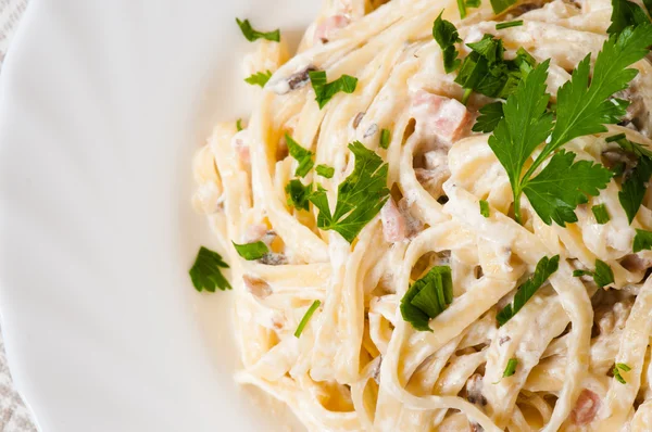 Spaghetti. Fettuccine carbonara in een witte kom, gegarneerd met spek, champignons en peterselie — Stockfoto