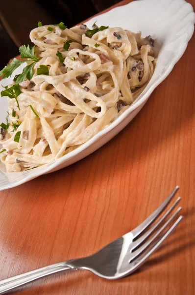 Spaghetti. Fettuccine carbonara in een witte kom, gegarneerd met spek, champignons en peterselie. — Stockfoto