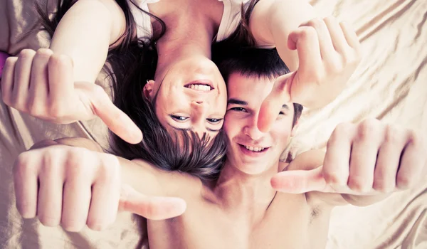 Pareja feliz acostada en la cama con los pulgares arriba — Foto de Stock