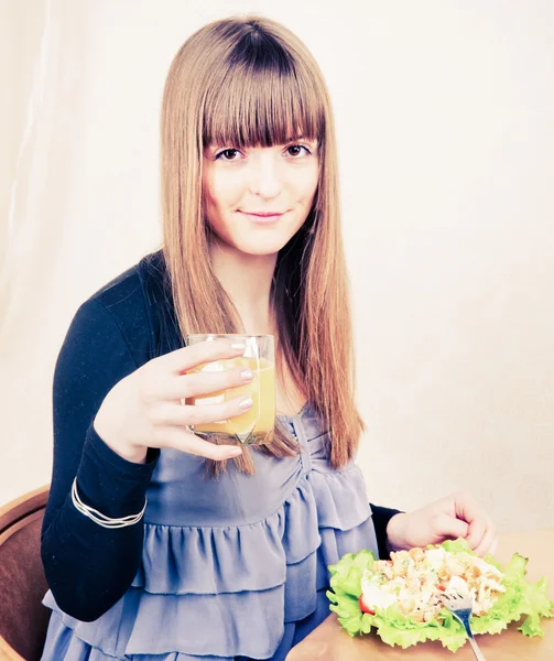 Ung kvinna sitter vid bord med frukost, dricka orange j — Stockfoto
