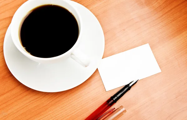 Taza de café, pedazo de papel y pluma en la mesa de madera — Foto de Stock