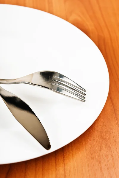 Tenedor y cuchillo con plato blanco sobre fondo de madera — Foto de Stock