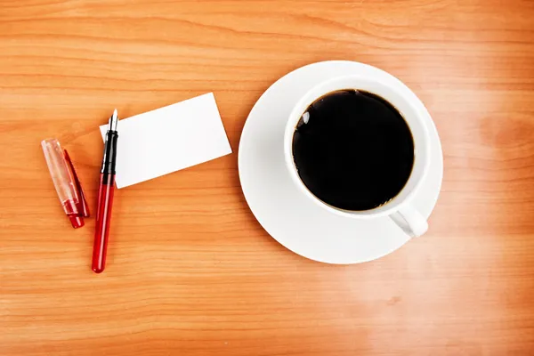 Taza de café, pedazo de papel y pluma en la mesa de madera — Foto de Stock