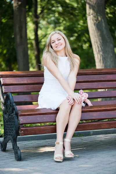 Jovem mulher sentada no banco no parque — Fotografia de Stock