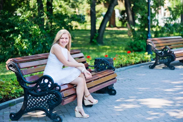 Ung kvinde sidder på bænken i parken Stock-foto