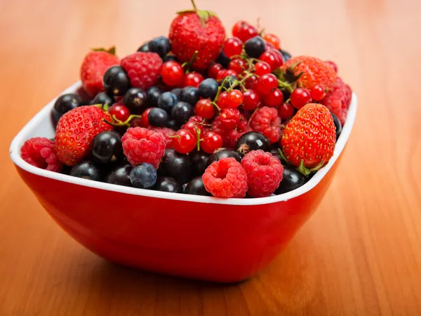 Arándanos, fresas, frambuesas, grosellas negras y rojas en tazón rojo sobre la mesa —  Fotos de Stock