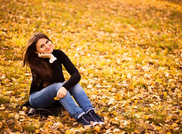 Jovem mulher senta-se em folhas no parque de outono — Fotografia de Stock
