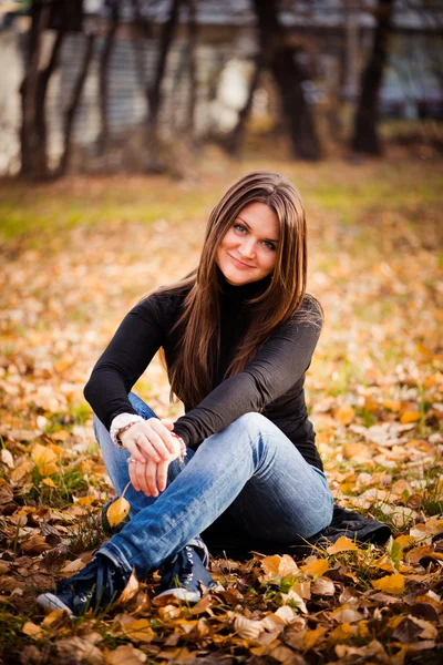 Jovem mulher senta-se em folhas no parque de outono — Fotografia de Stock