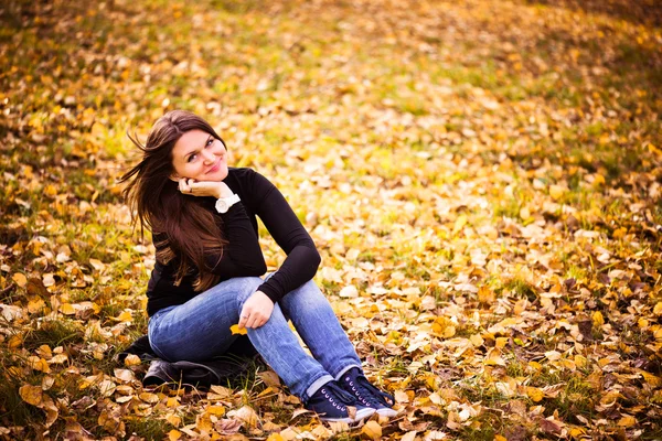 Giovane donna siede sulle foglie nel parco autunnale — Foto Stock