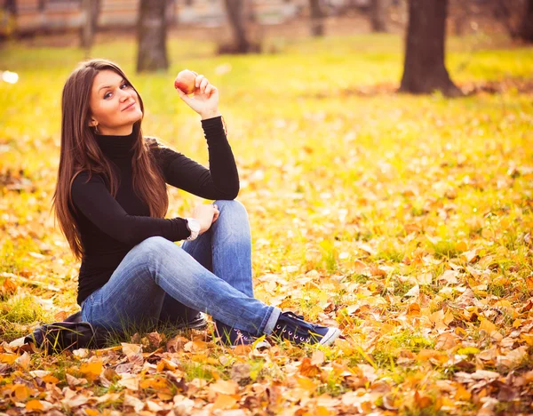 Portrait of beautiful young woman with apple in autumn park — Stock Photo, Image
