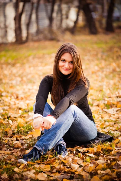 Young woman sits on leaves in autumn park — Stock Photo, Image