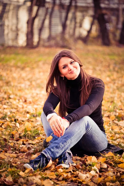 Mujer joven se sienta en hojas en el parque de otoño — Foto de Stock