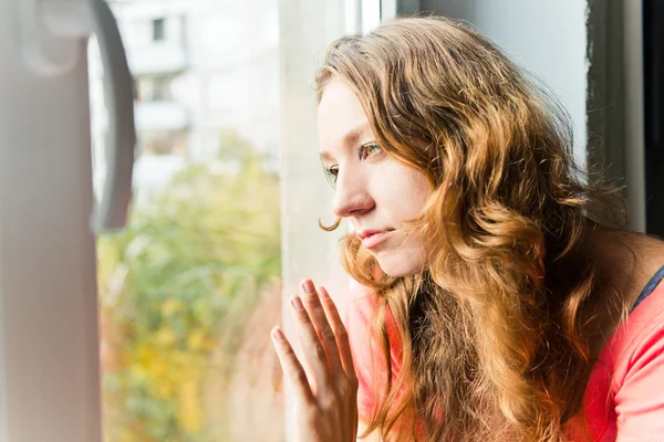 Beautiful young woman is sad at the window — Stock Photo, Image