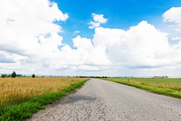 Asfaltową drogą przez zielone pola i chmury — Zdjęcie stockowe