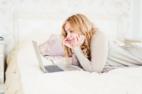 Šťastná Mladá blondýnka ležící na posteli, pomocí přenosného počítače — Stock fotografie