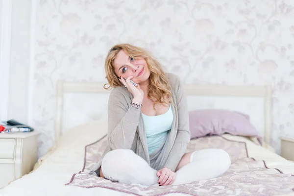 Блондинка, лежащая на кровати и звонящая — стоковое фото