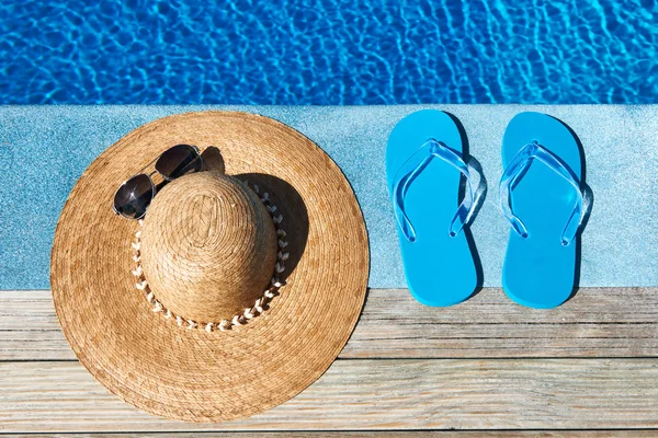 Pantoufles bleues et chapeau au bord d'une piscine — Photo