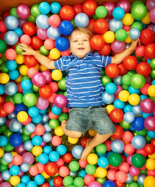 Criança feliz brincando com bolas plásticas coloridas — Fotografia de Stock