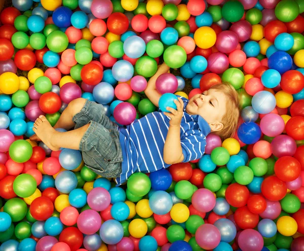 Niño feliz jugando con bolas de plástico de colores — Foto de Stock