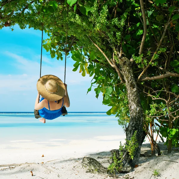 Vrouw in blauwe jurk swingende op strand — Stockfoto