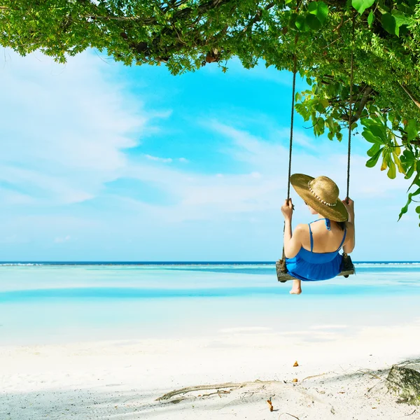 Vrouw in blauwe jurk swingende op strand — Stockfoto