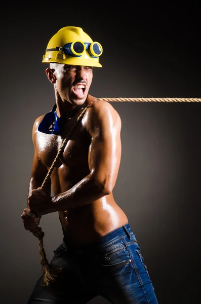 Constructor desnudo tirando de la cuerda en la oscuridad —  Fotos de Stock