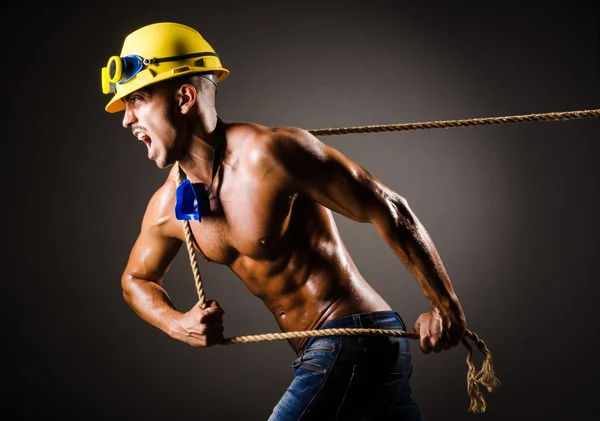 Constructor desnudo tirando de la cuerda en la oscuridad — Foto de Stock