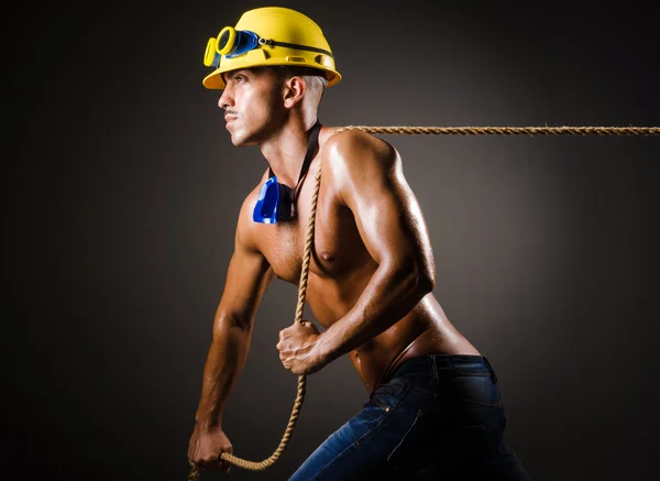 Голый строитель тянет веревку в темноте — стоковое фото