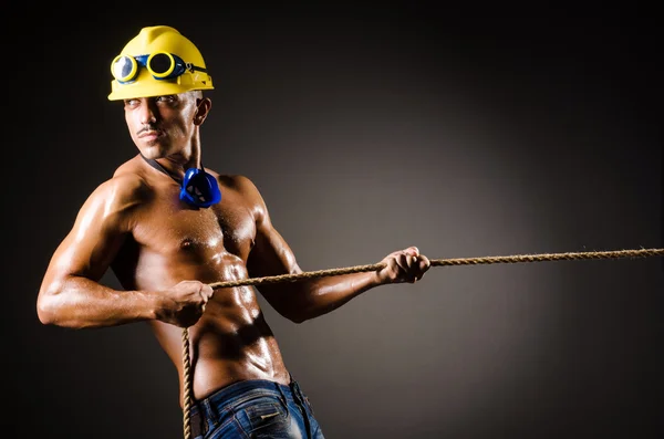 Constructor desnudo tirando de la cuerda en la oscuridad —  Fotos de Stock
