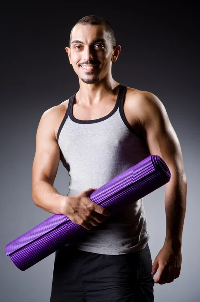 Muscular man with mat in studio — Stock Photo, Image