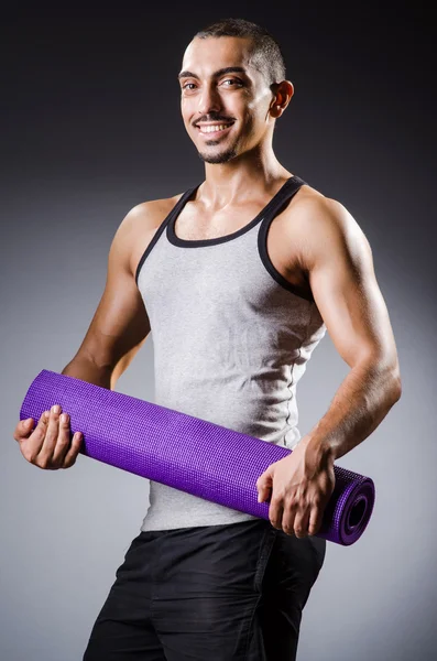 Muscular man with mat in studio — Stock Photo, Image