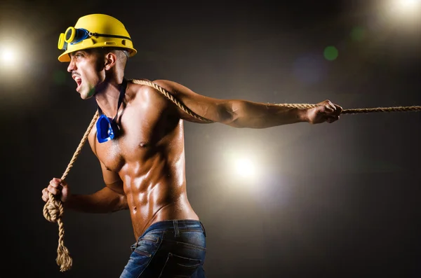 Constructor desnudo tirando de la cuerda en la oscuridad — Foto de Stock